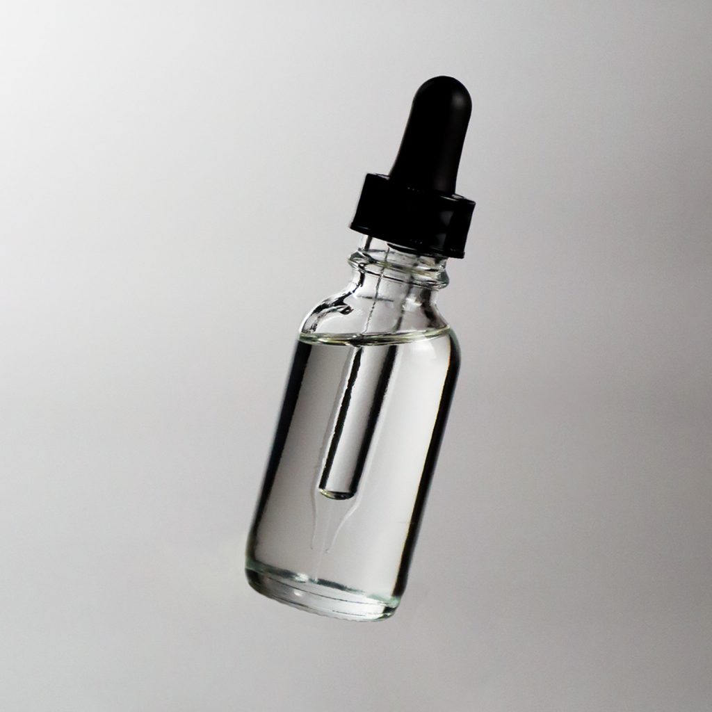 Dropper bottle with clear cosmetic fluid on white/grey background